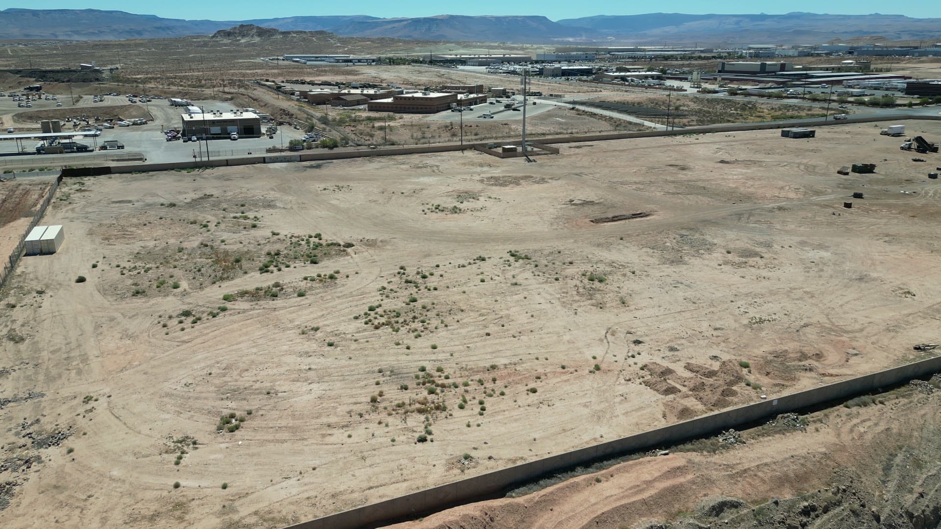 Aerial view of the cleared industrial park site with neighboring industrial buildings and red-rock mesas in the distance